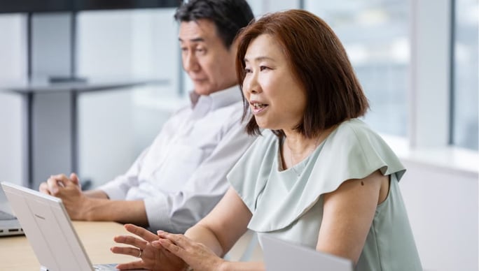 会議室で発言する社員の女性と、その様子を聞く男性社員。NTTデータMSEの事例インタビューの一場面(写真)