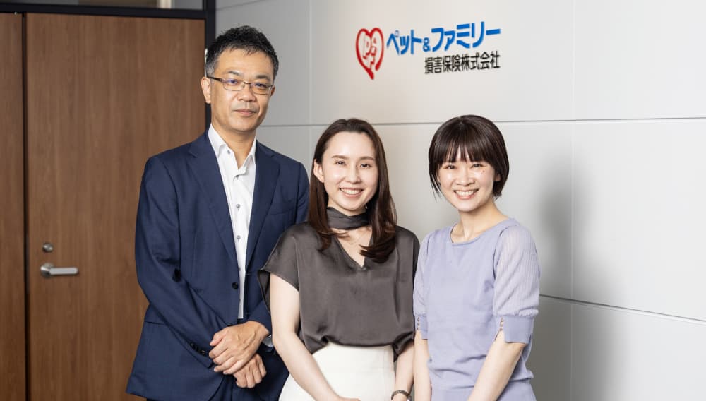 ペット＆ファミリー損害保険株式会社の社内にて、インタビューを受けた社員が社名ロゴの前で並んで立つ写真