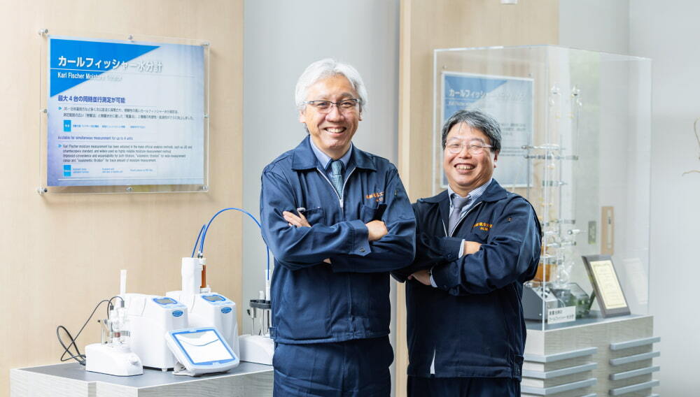 さまざまな分析計測機器の前に立つ山口様と松岡様）