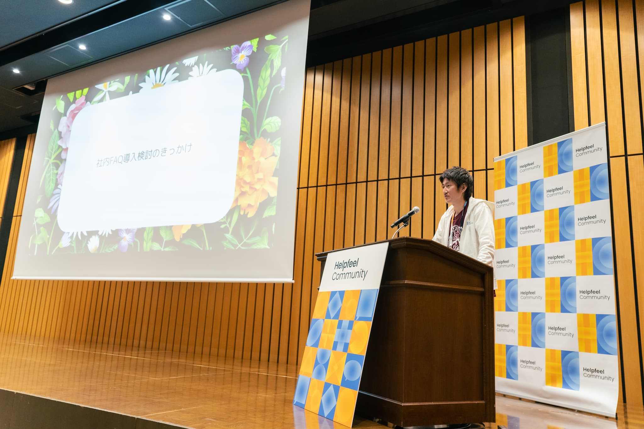新山様が登壇。画面には「社内FAQ導入のきっかけ」の文字