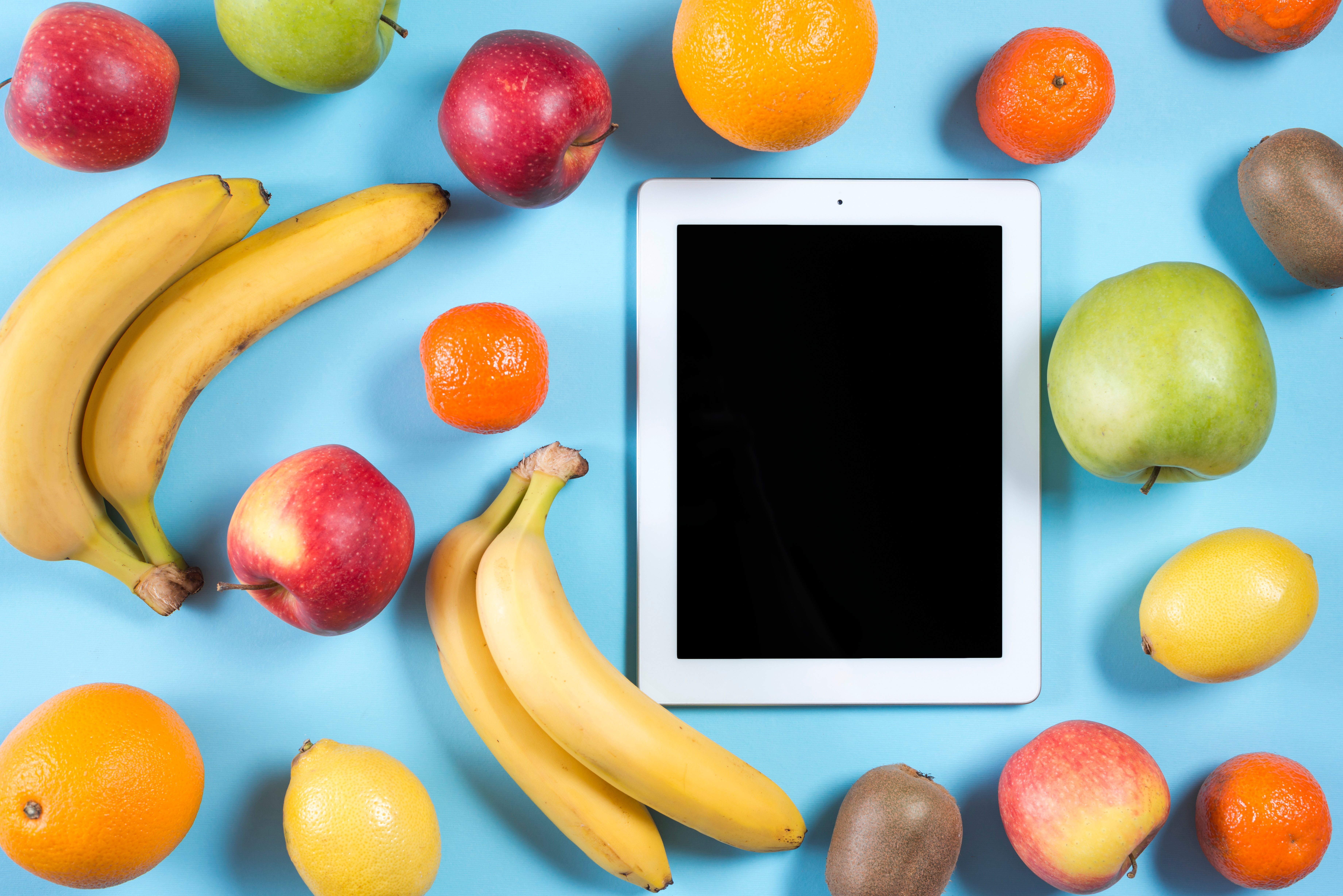 blank-digital-tablet-surrounded-with-whole-healthy-fruits-blue-background