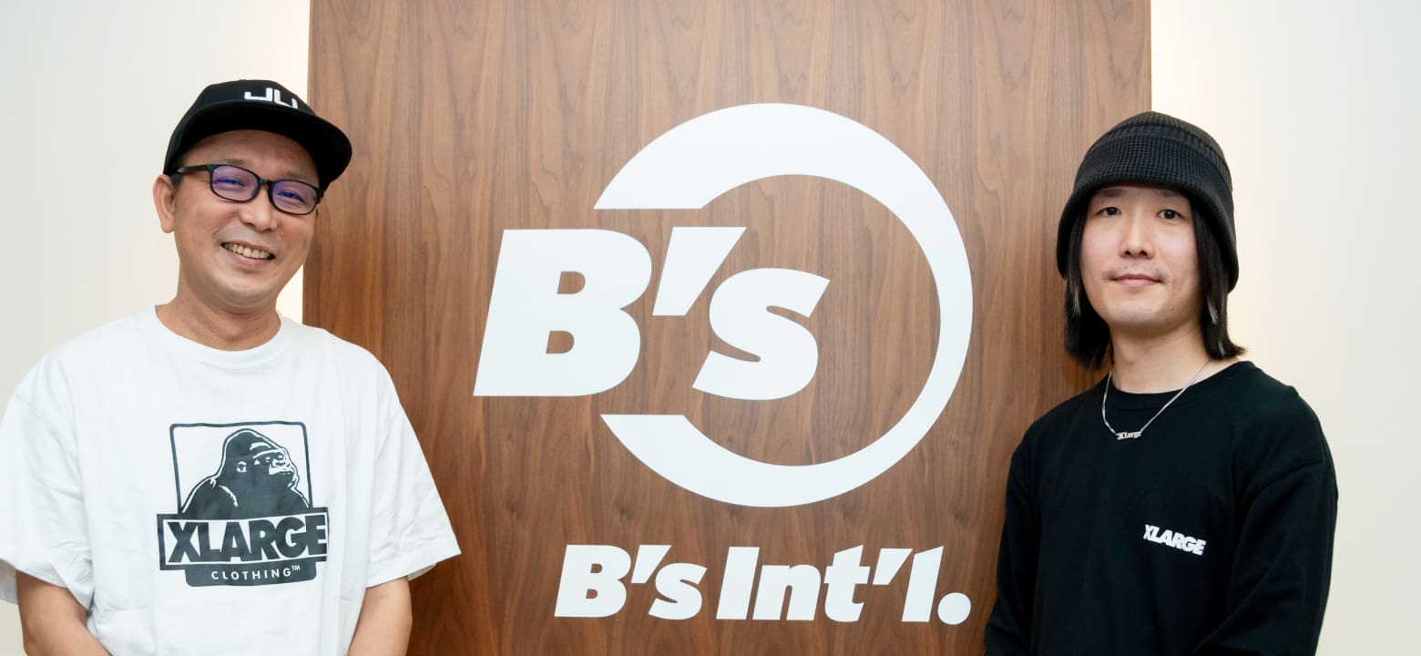 B'sと書かれた壁面の前に立つ男性2人