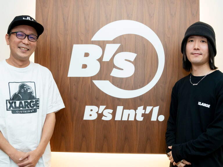 B'sと書かれた壁面の前に立つ男性2人