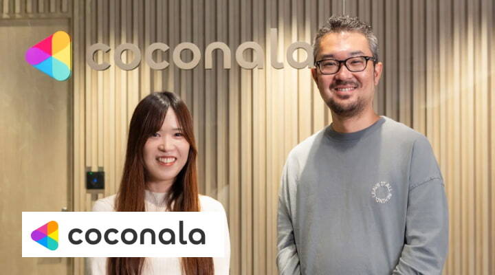 ココナラのロゴが掲げられたオフィスの前で、カジュアルな服装の男女社員が笑顔で並んで立っている。