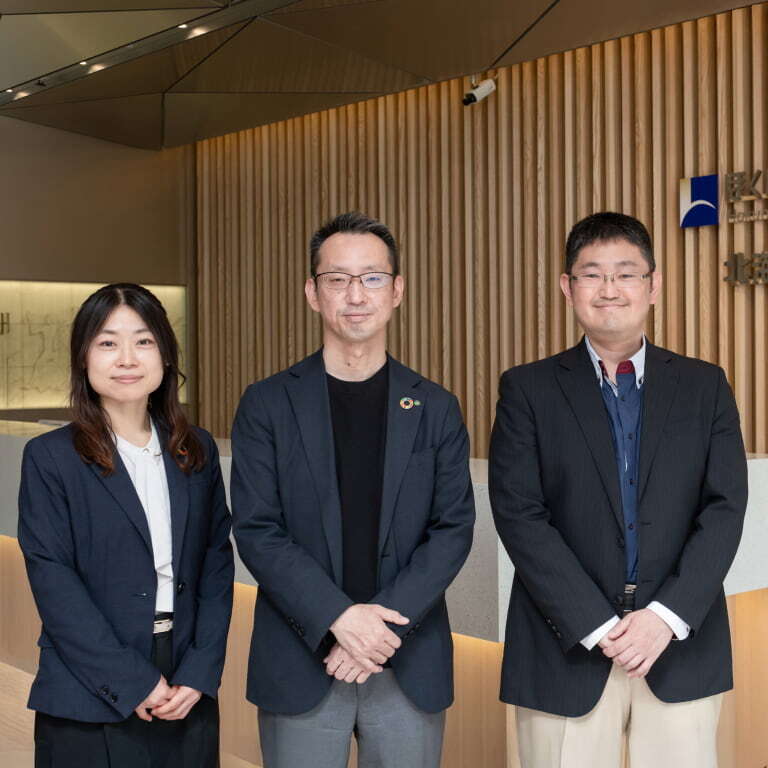 北海道銀行の行員３名が企業ロゴの前で立っている写真
