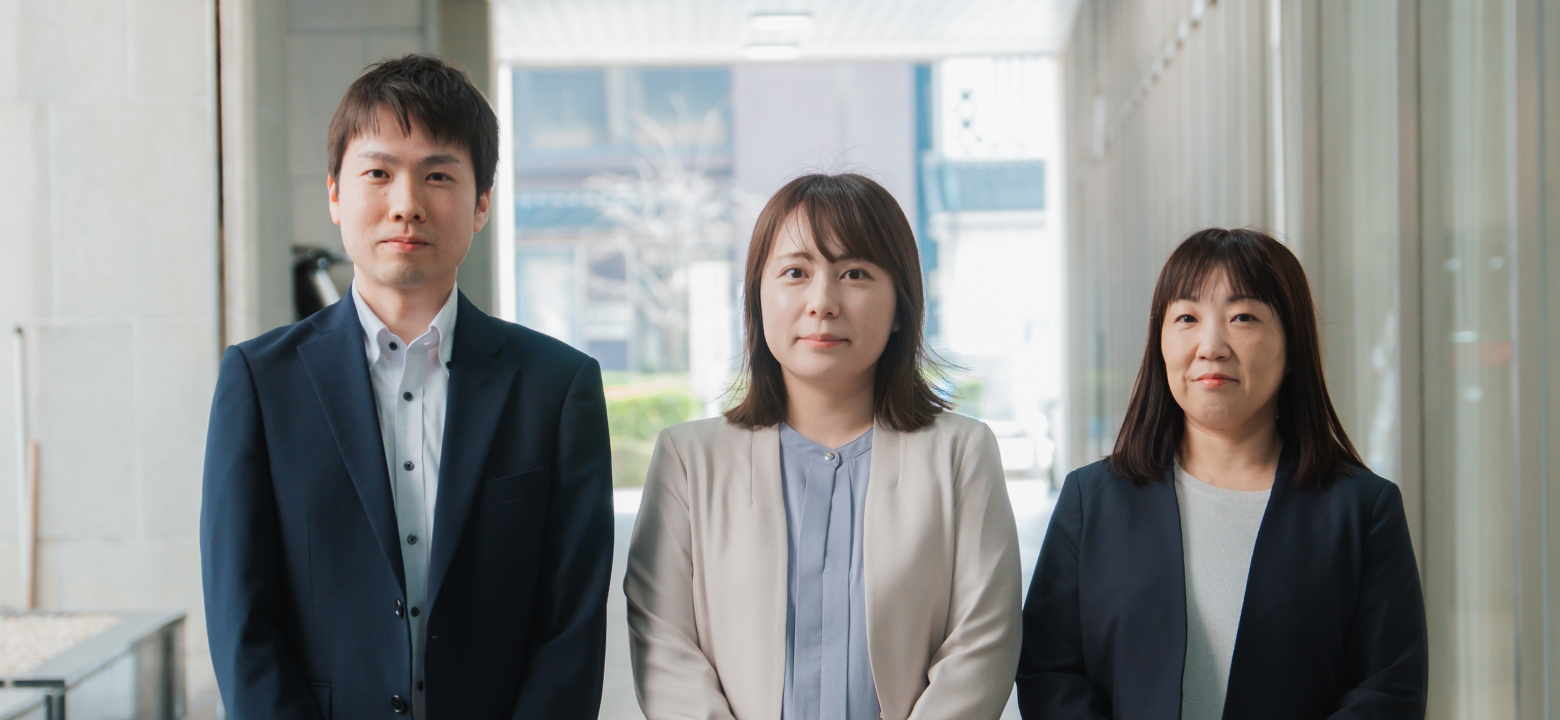 スーツやオフィスカジュアルを着用した、笑顔の男女3名が並んでいる写真