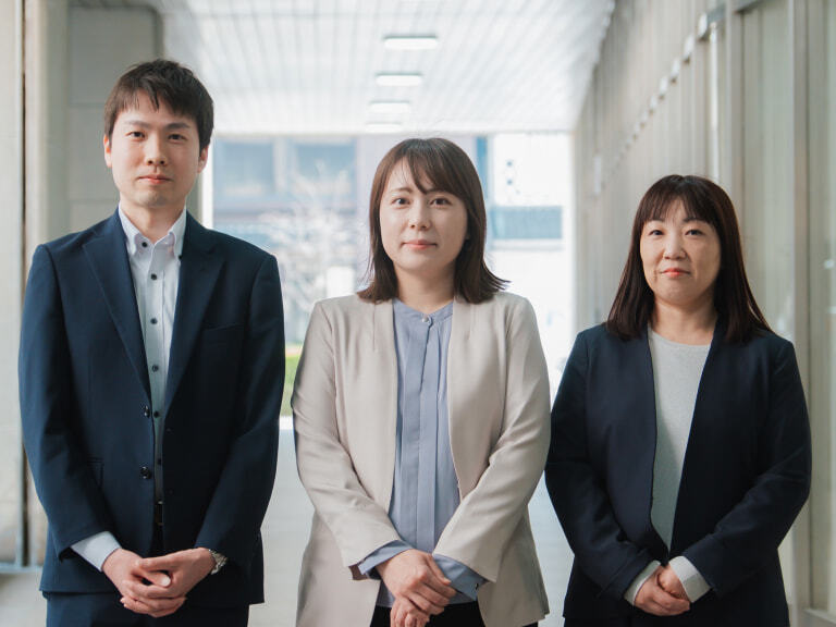 スーツやオフィスカジュアルを着用した、笑顔の男女3名が並んでいる写真