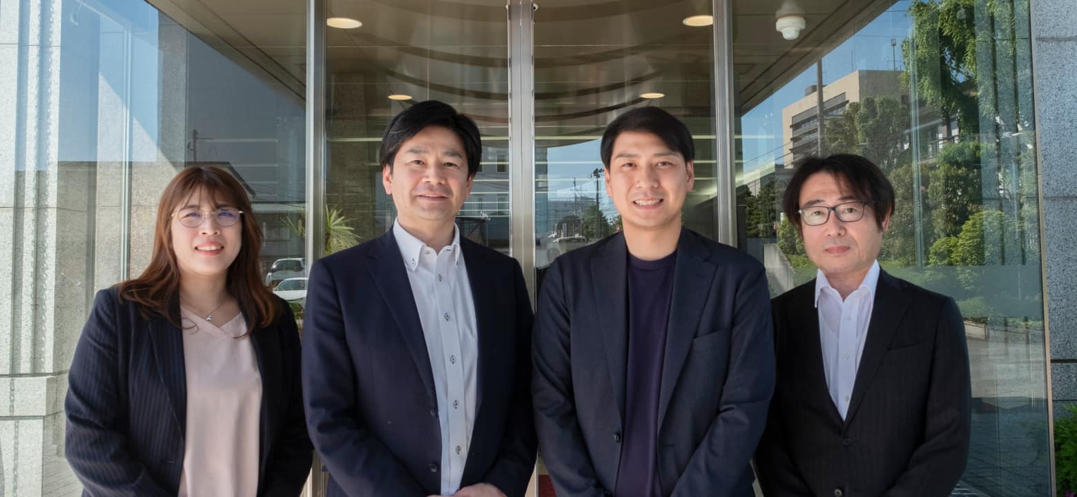 スーツを着用した4人が会社の玄関に立っている写真