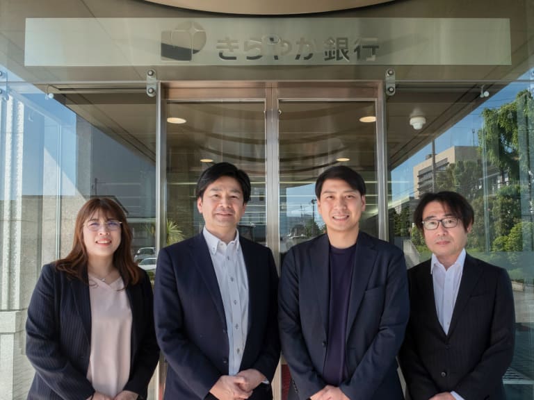 スーツを着用した4人が会社の玄関に立っている写真