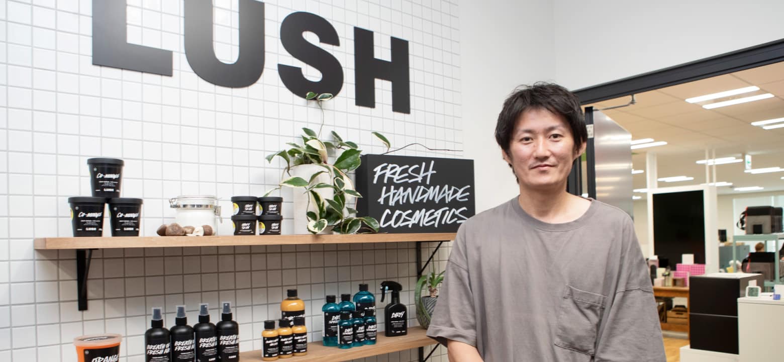 並べられた商品の横に立つ男性。壁にLUSHの文字