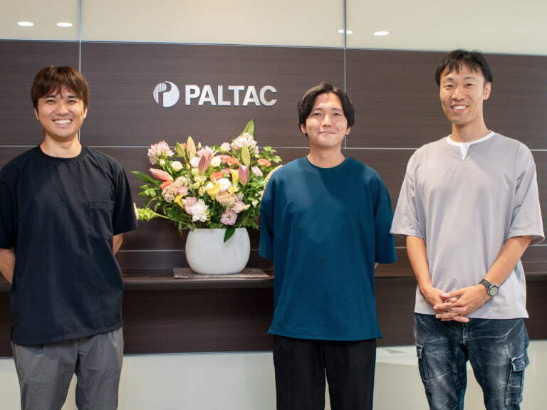 PALTACのロゴが書かれた壁の前で微笑む3人の男性