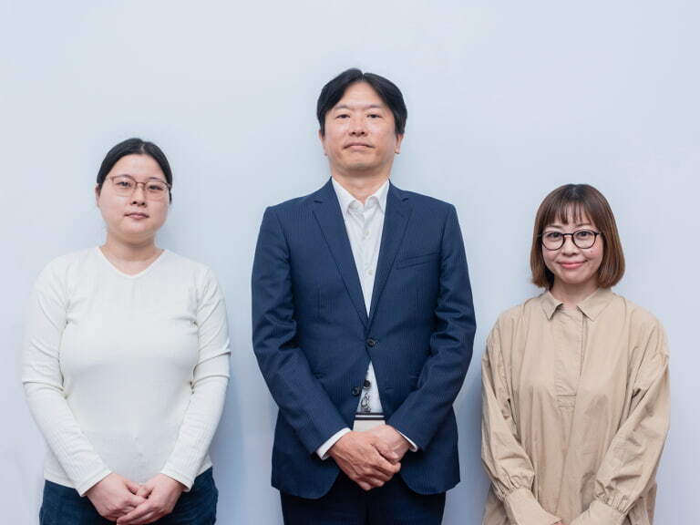 白い壁の前に立つ2人の女性と1人の男性