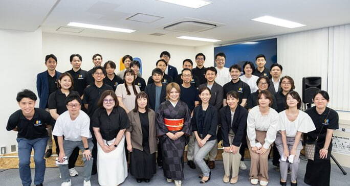 地銀AIプロジェクトのメンバーによる集合写真。オフィスにて、中央に着物姿の女性、周囲にプロジェクトチームの男女が並んでいる様子。