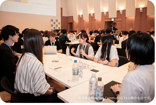 広いイベントホールに集まった多数の参加者が、グループごとに分かれて活発に議論を行っている全体像。