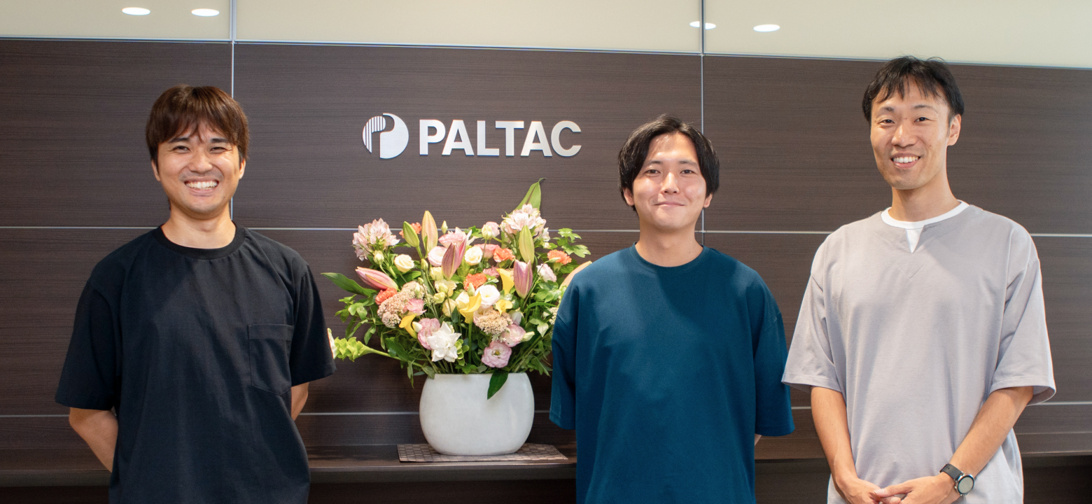 壁にPALTACと書かれた場所に男性が3名並んでいる